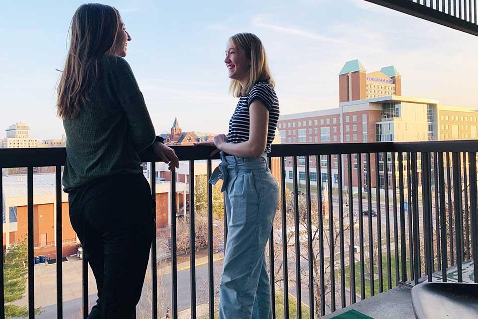 Two female students standing on a balcony overlooking campus